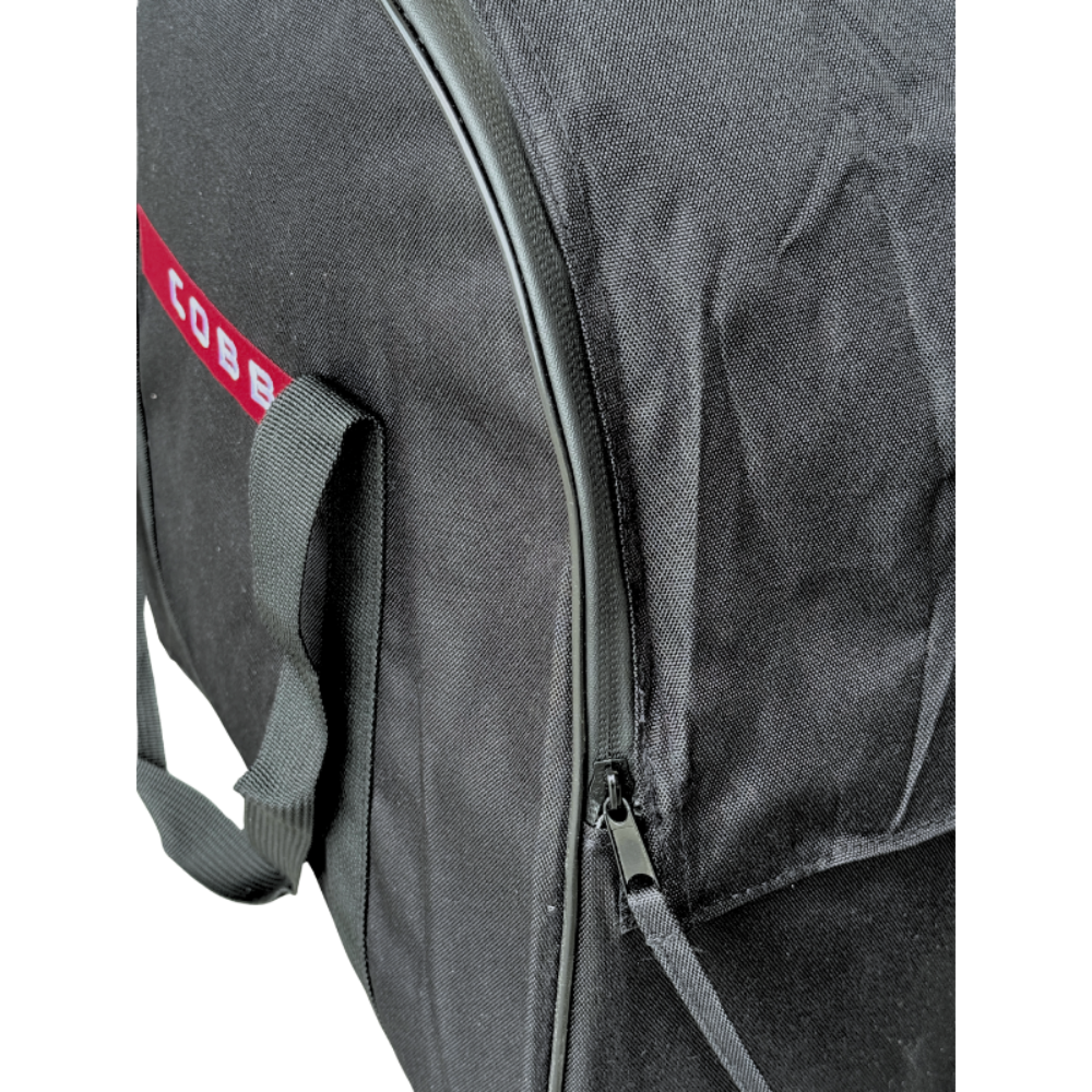 Close-up of a black fabric bag with a red and white COBB logo patch, a gray webbed handle, and a dark zipper.