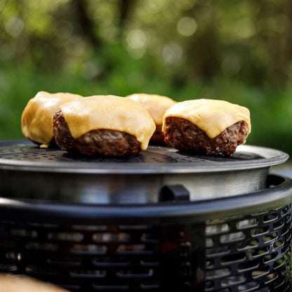Beef burgers with cheese on a COBB grill over a natural outdoor setting