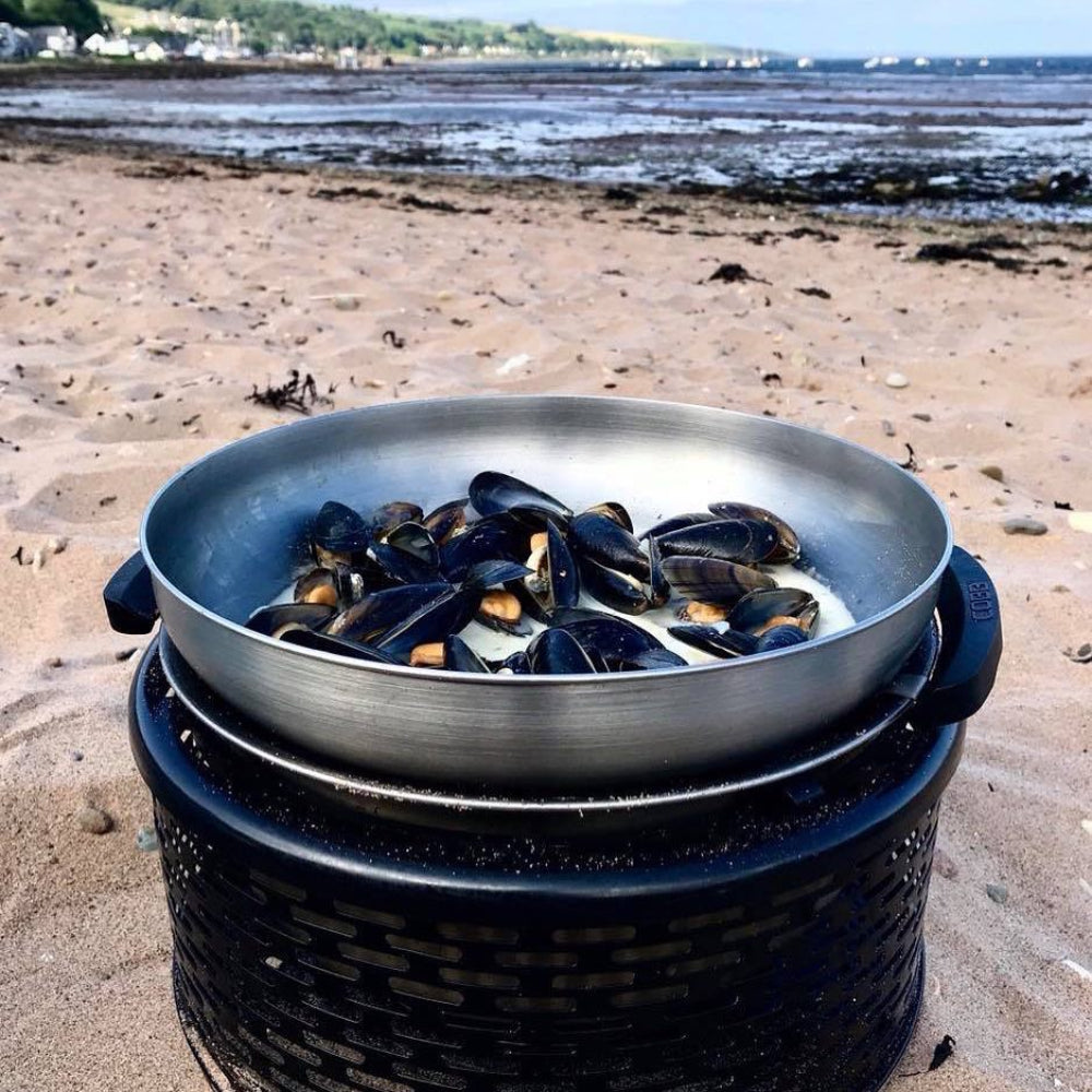Frying pan with mussels on a portable 'COBB' grill on a beach