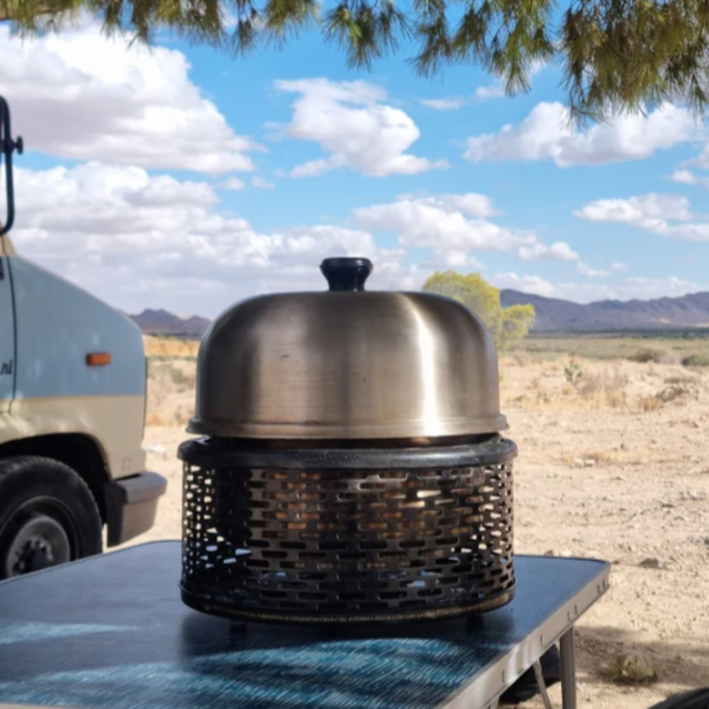 Stainless steel portable grill on a table with a desert landscape and camper van in the background