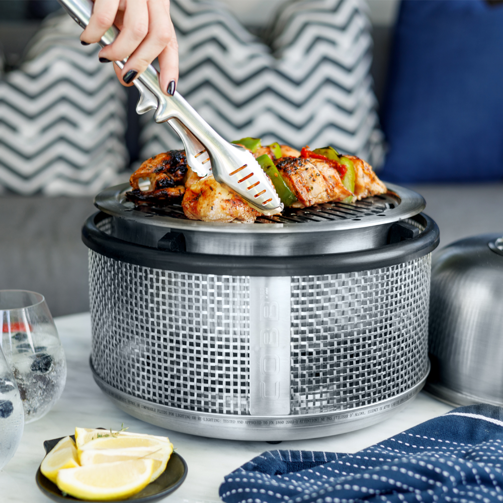 COBB Portable Cooker on a patio table cooking chicken skewers