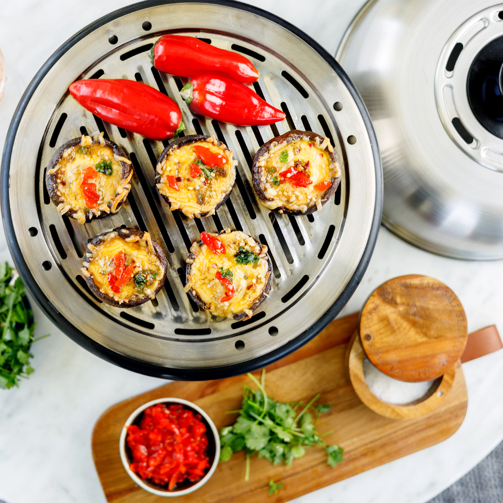 COBB Portable Cooker on a patio table cooking stuffed mushrooms and peppers