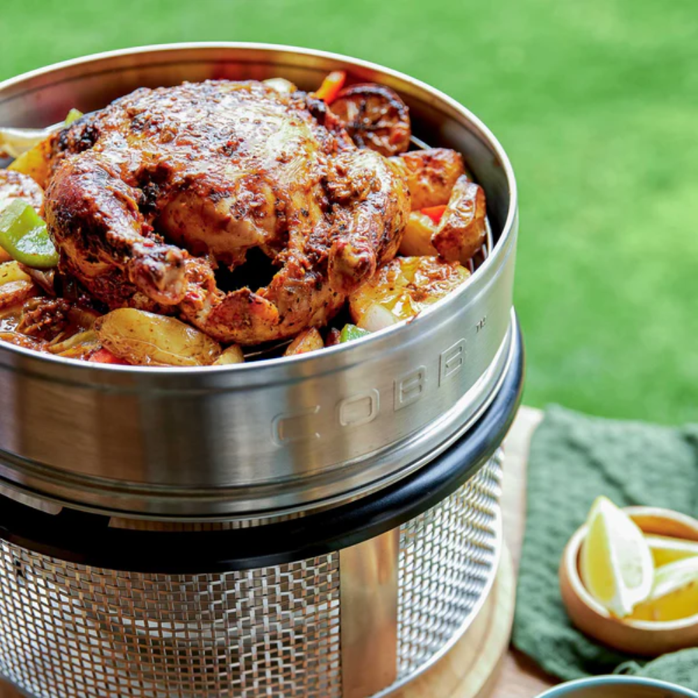 Cooked chicken and vegetables in a COBB grill on a green grass background.