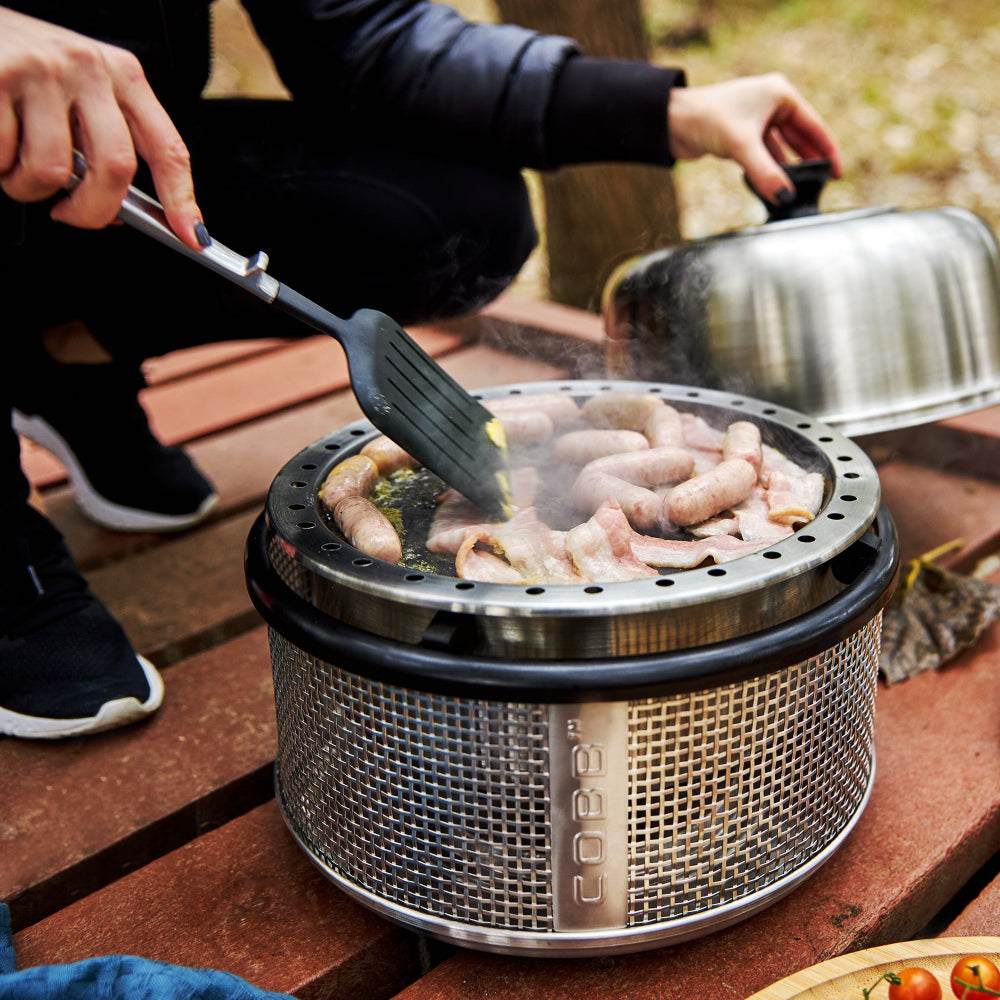 Person cooking on a portable grill with food and a spatula outdoors.