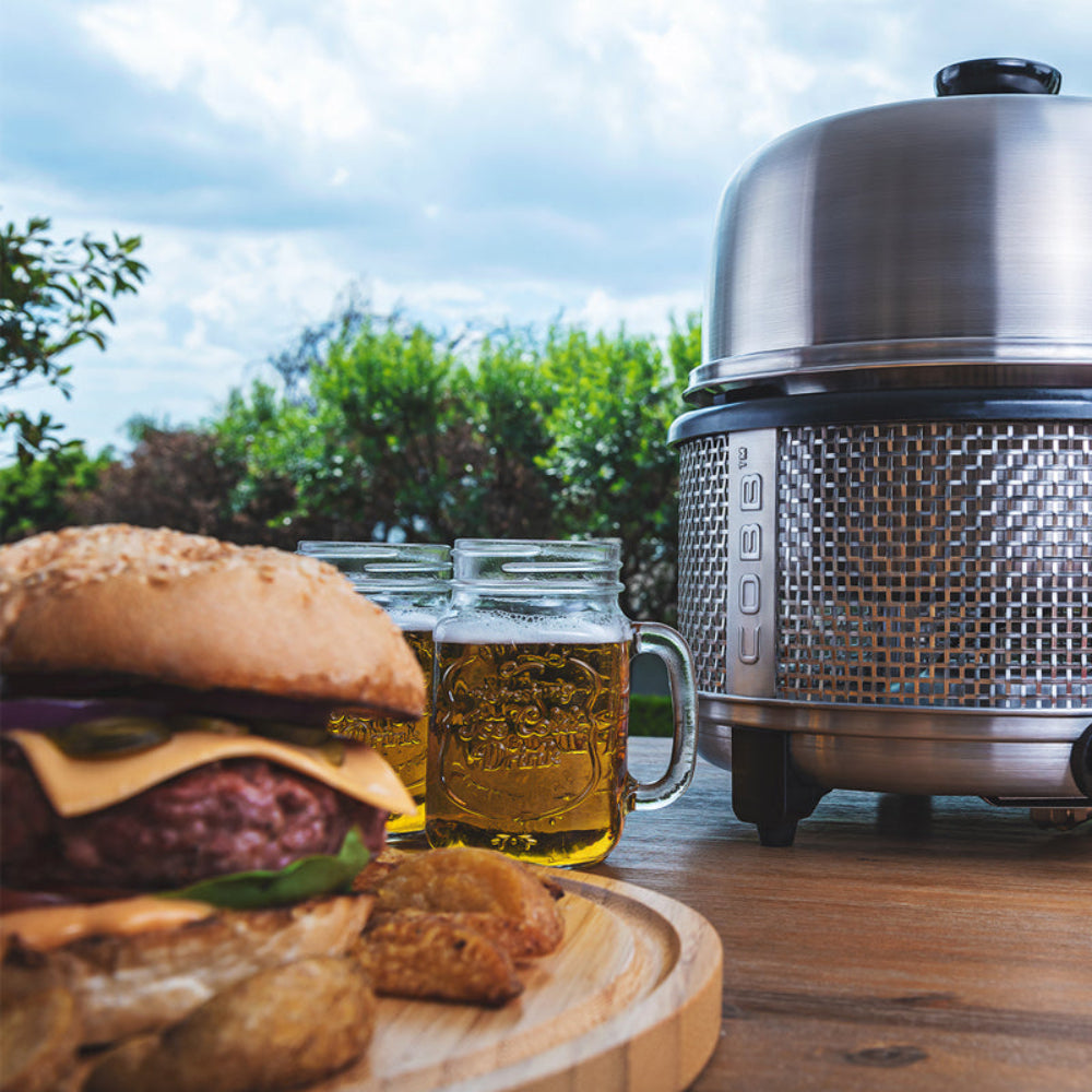 COBB portable gas cooker on wooden table with hamburgers and beer glasses