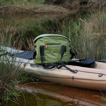 Green Anywhere bag on a kayak by a body of water with grass and plants in the background