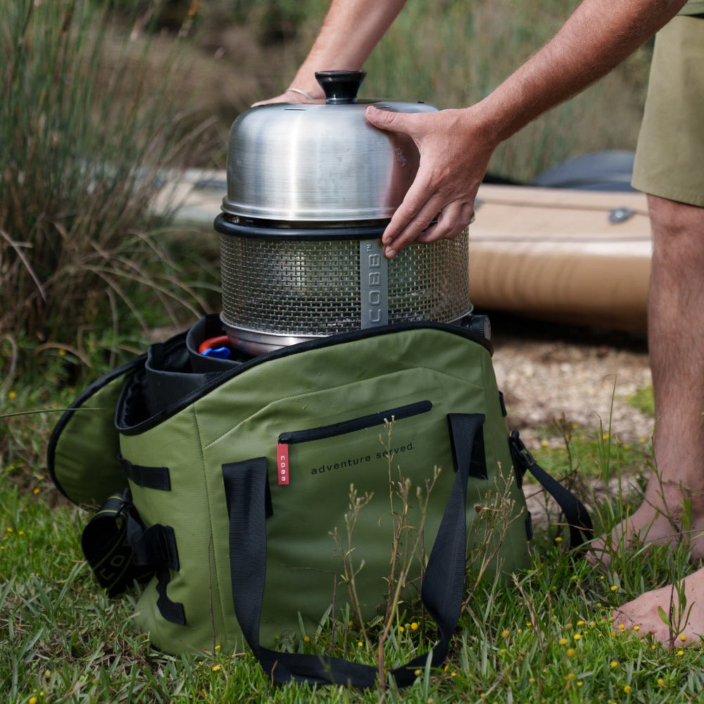 Person placing a COBB Grill in a green bag outdoors.
