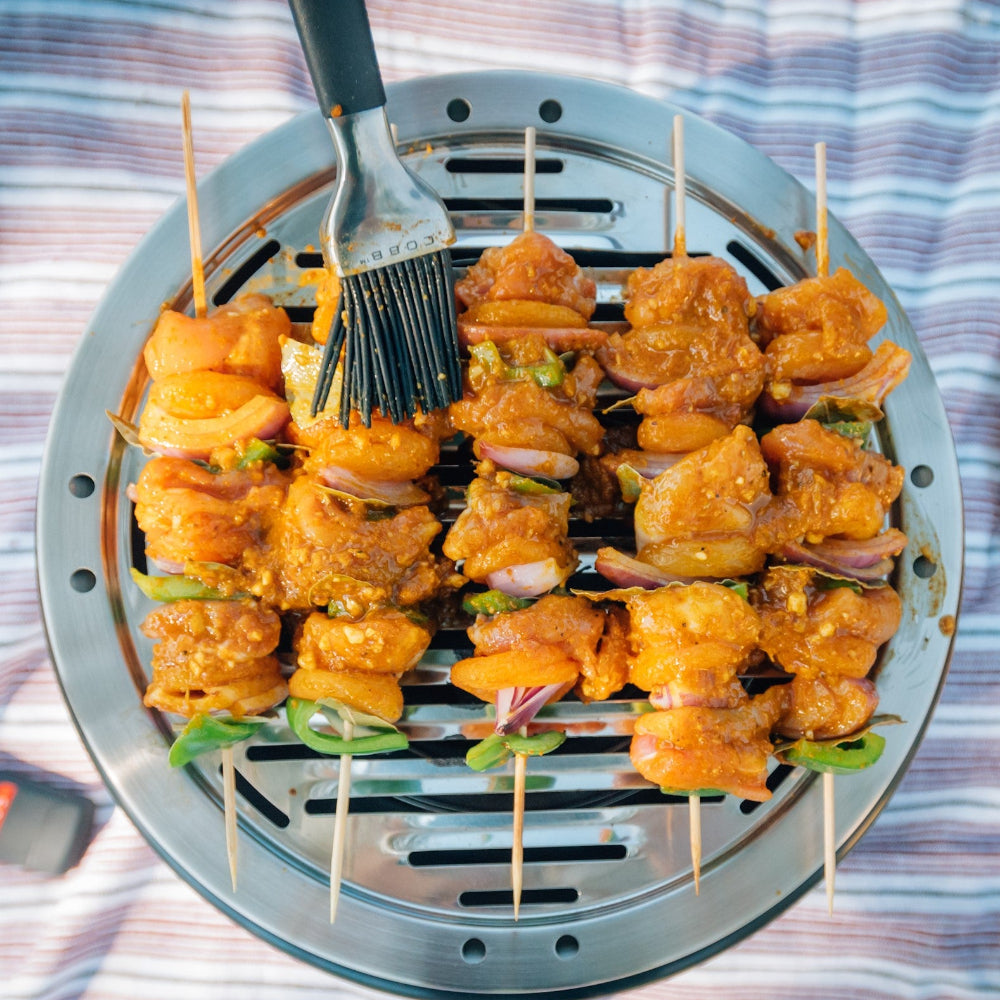 Skewers of marinated meat being brushed with a basting brush over a COBB BBQ.