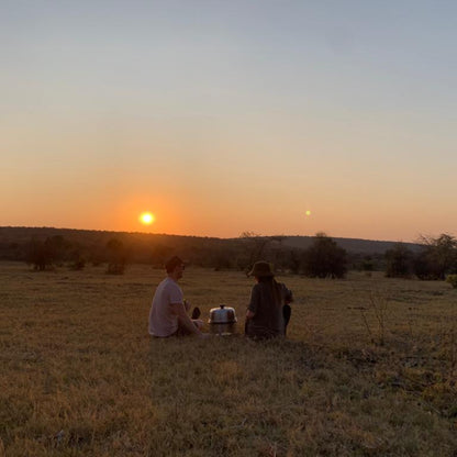 Two people sitting on a grassy field watching the sunset with COBB Cooking.