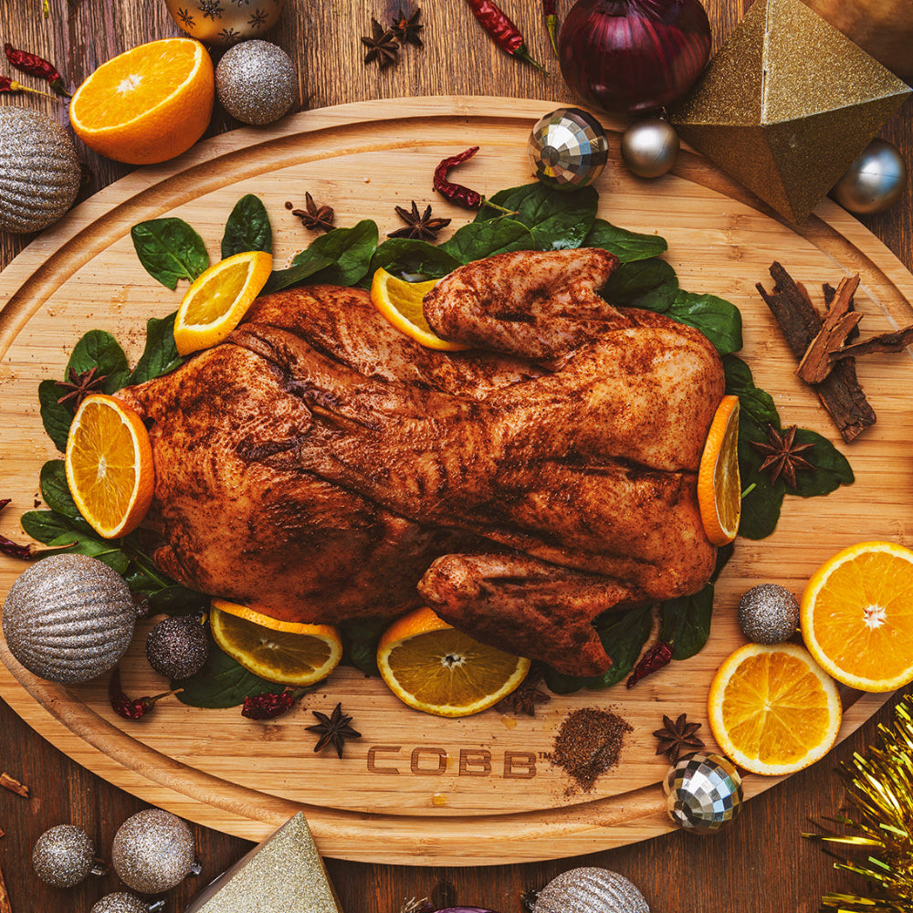 Roast chicken on a wooden board with oranges and herbs, surrounded by festive decorations.