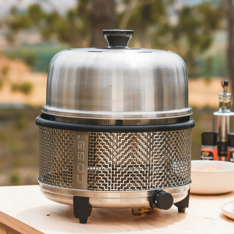 gas Cobb grill on a table with a blurred outdoor background