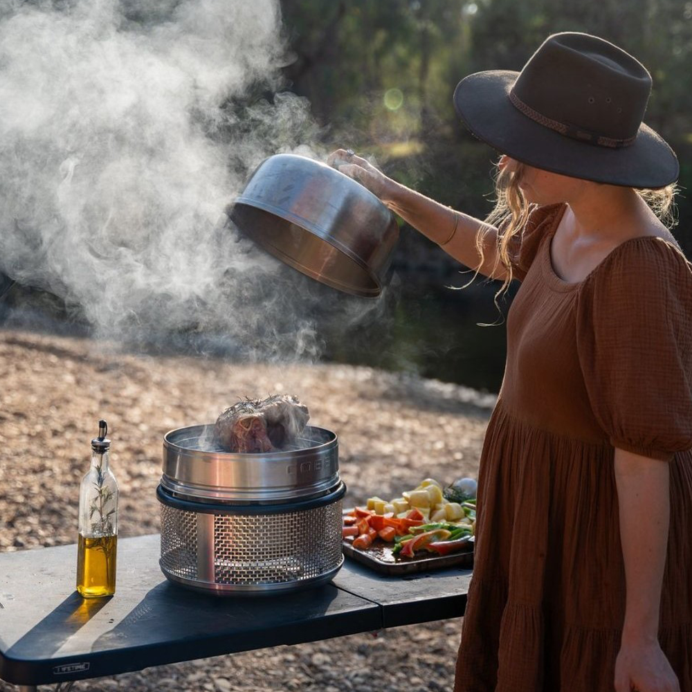 Person cooking outdoors with a COBB portable grill and food items on a natural background