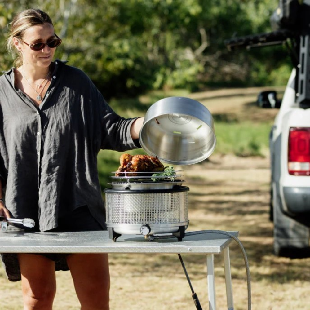 Woman cooking outdoors using a portable grill with a truck in the background