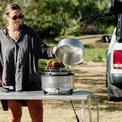 Woman cooking outdoors using a portable grill with a truck in the background