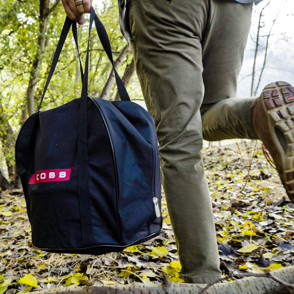 Person walking through a forest carrying a black bag with a red 'COBB' logo.